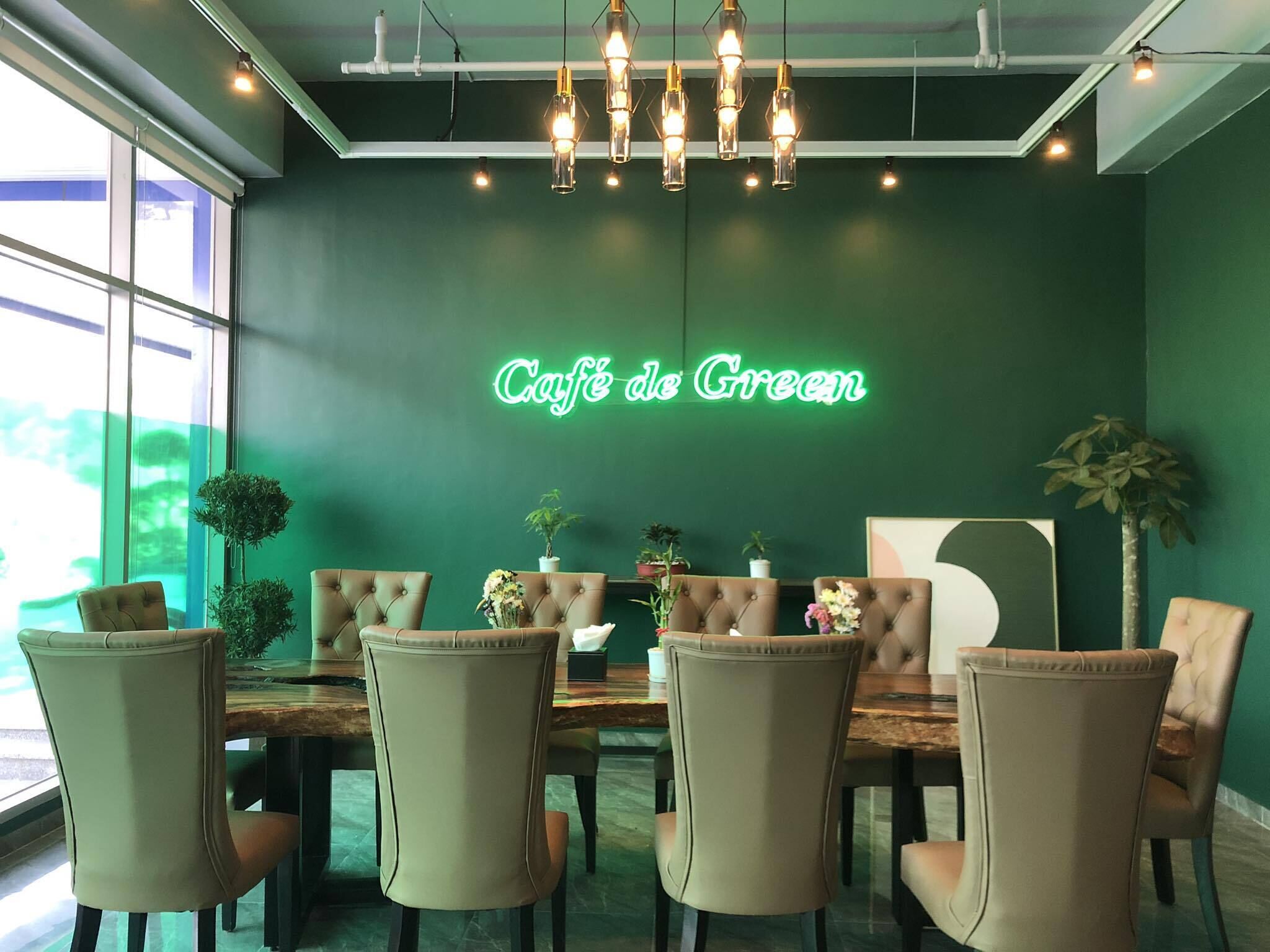 L’intérieur d’un café, avec une enseigne au néon indiquant « Café de Green », une table en bois, des chaises recouvertes d’un tissu beige et des lampes suspendues.