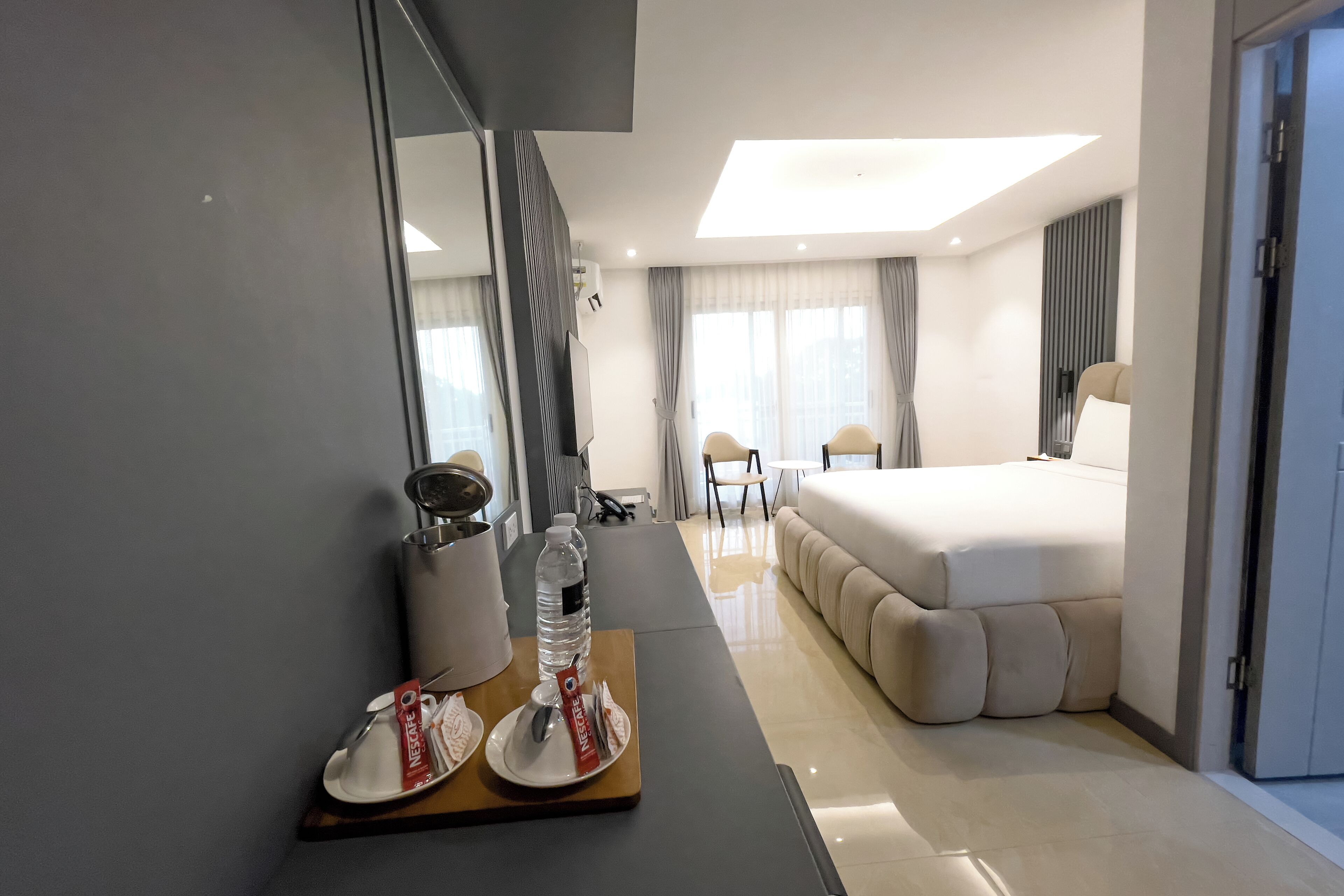 Een moderne hotelkamer met een groot bed, een nachtkastje met een waterfles en een bord eten, een stoel en een bureau met een spiegel.