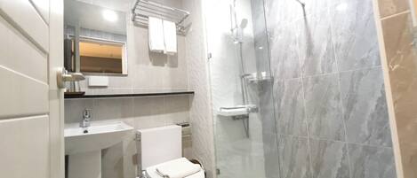 Un baño moderno con ducha de vidrio, lavamanos blanco y un inodoro.