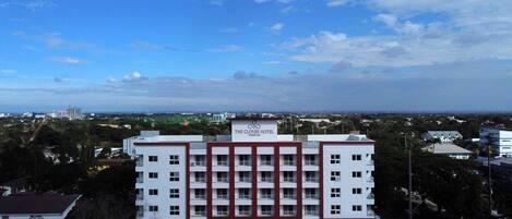 A multi-story hotel with a red and white facade, a visible sign for 'The Clover Hotel', and a parking lot with several cars.