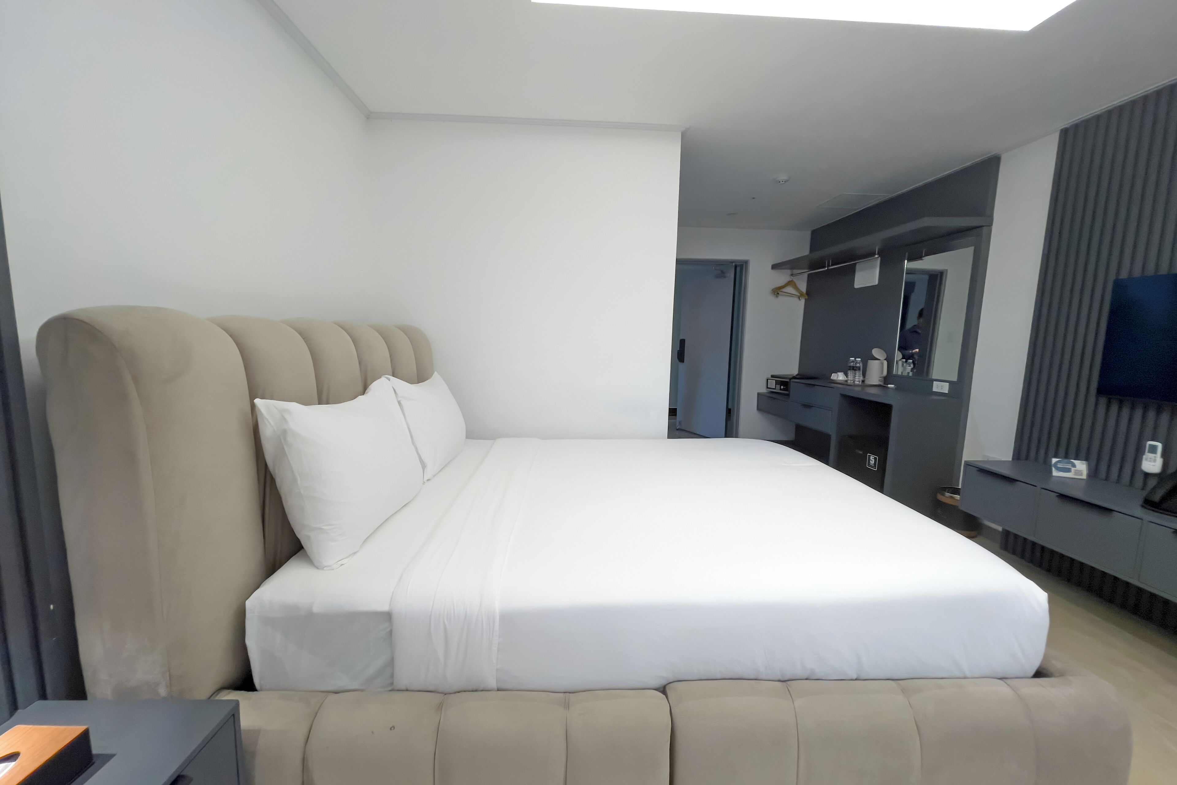Une chambre d’hôtel moderne dotée d’un grand lit, d’une télévision à écran plat, d’une coiffeuse avec miroir et d’un petit coin salon.