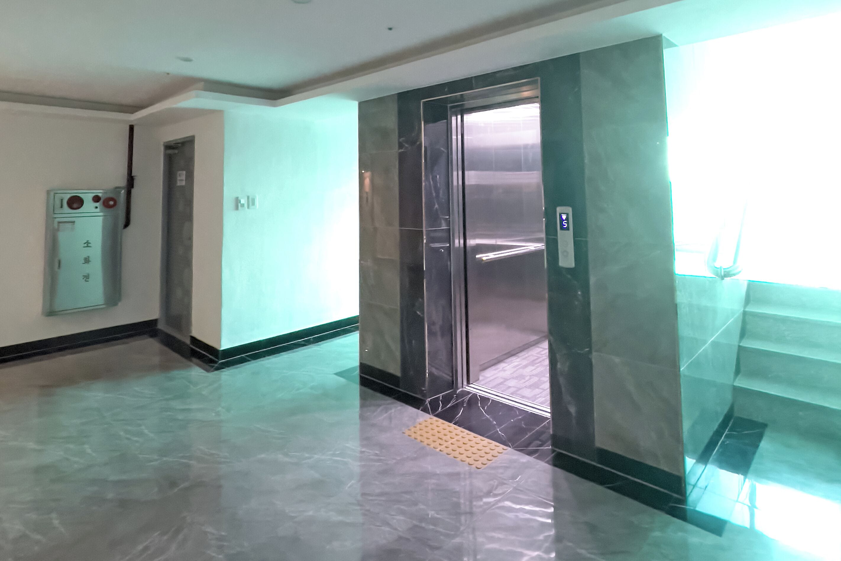 A modern elevator with a metallic finish, a control panel with buttons, and a clear glass door.
