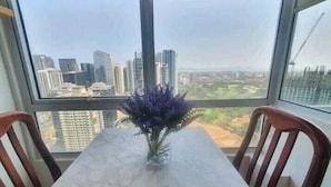 A dining area with a table and chairs, a vase with purple flowers, and a view of a cityscape through large windows. - Fort Victoria (Taguig)