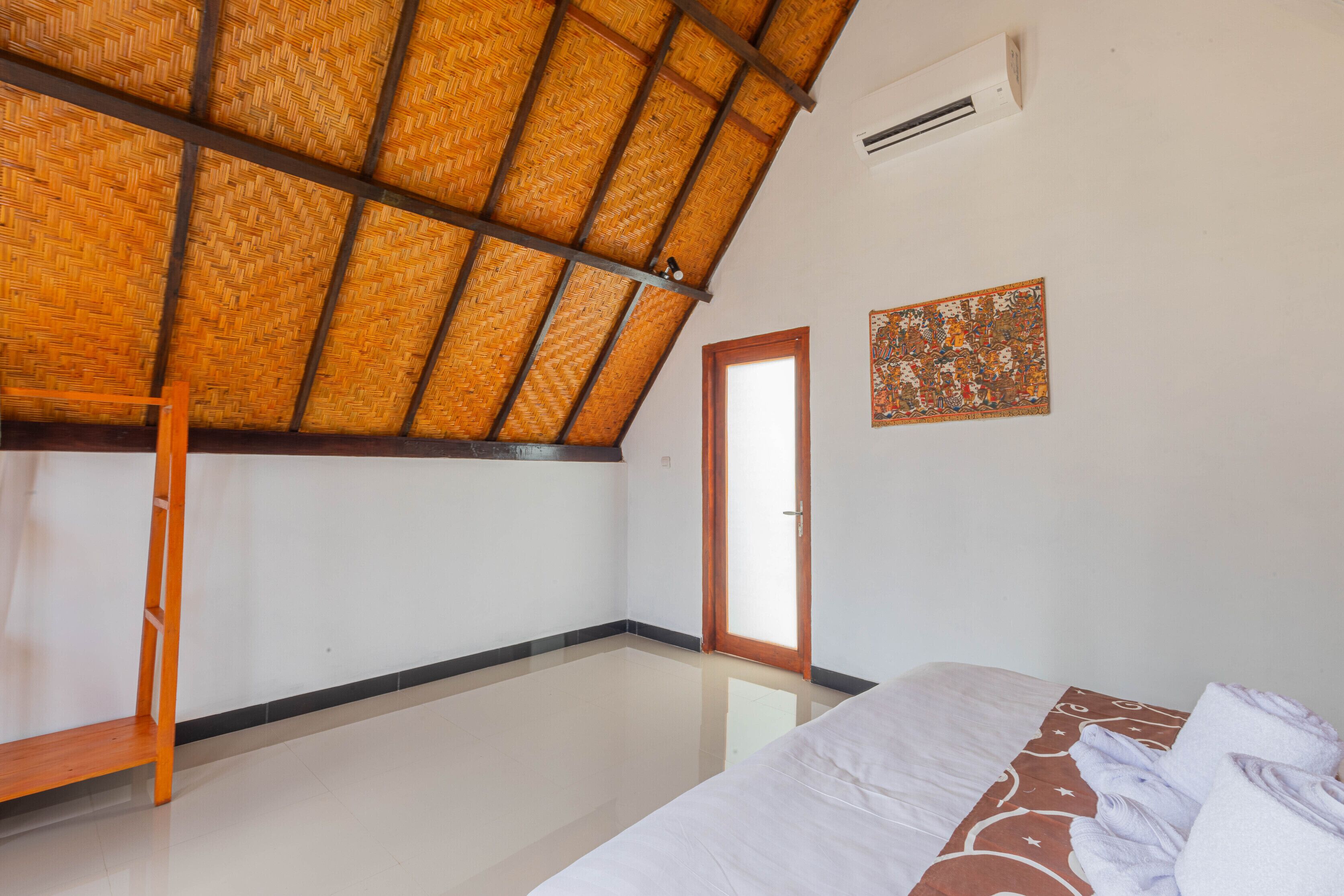 A room with a sloped ceiling, a bed with a patterned bedspread, a wooden ladder, and a door leading to another room.