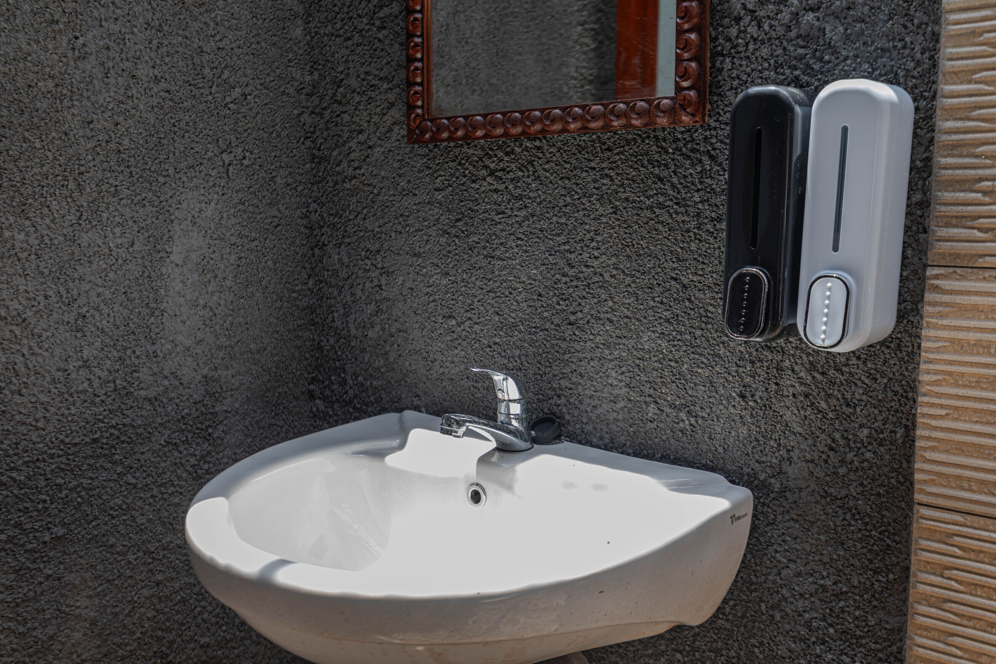 A bathroom sink with a mirror above it, a towel dispenser, and a soap dispenser.