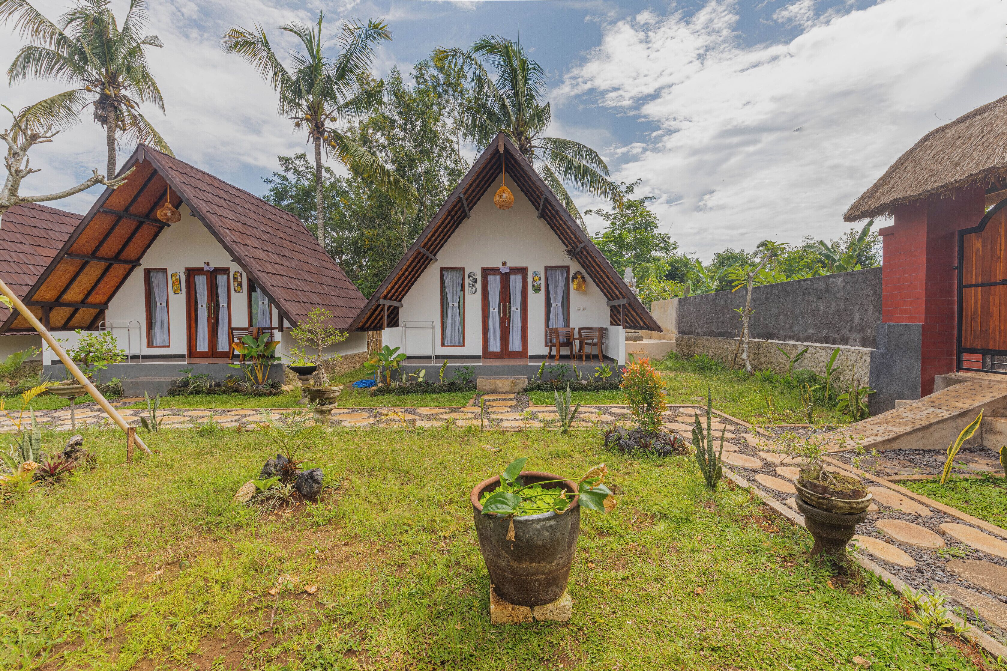 A bungalow with a thatched roof, surrounded by lush greenery and palm trees.
