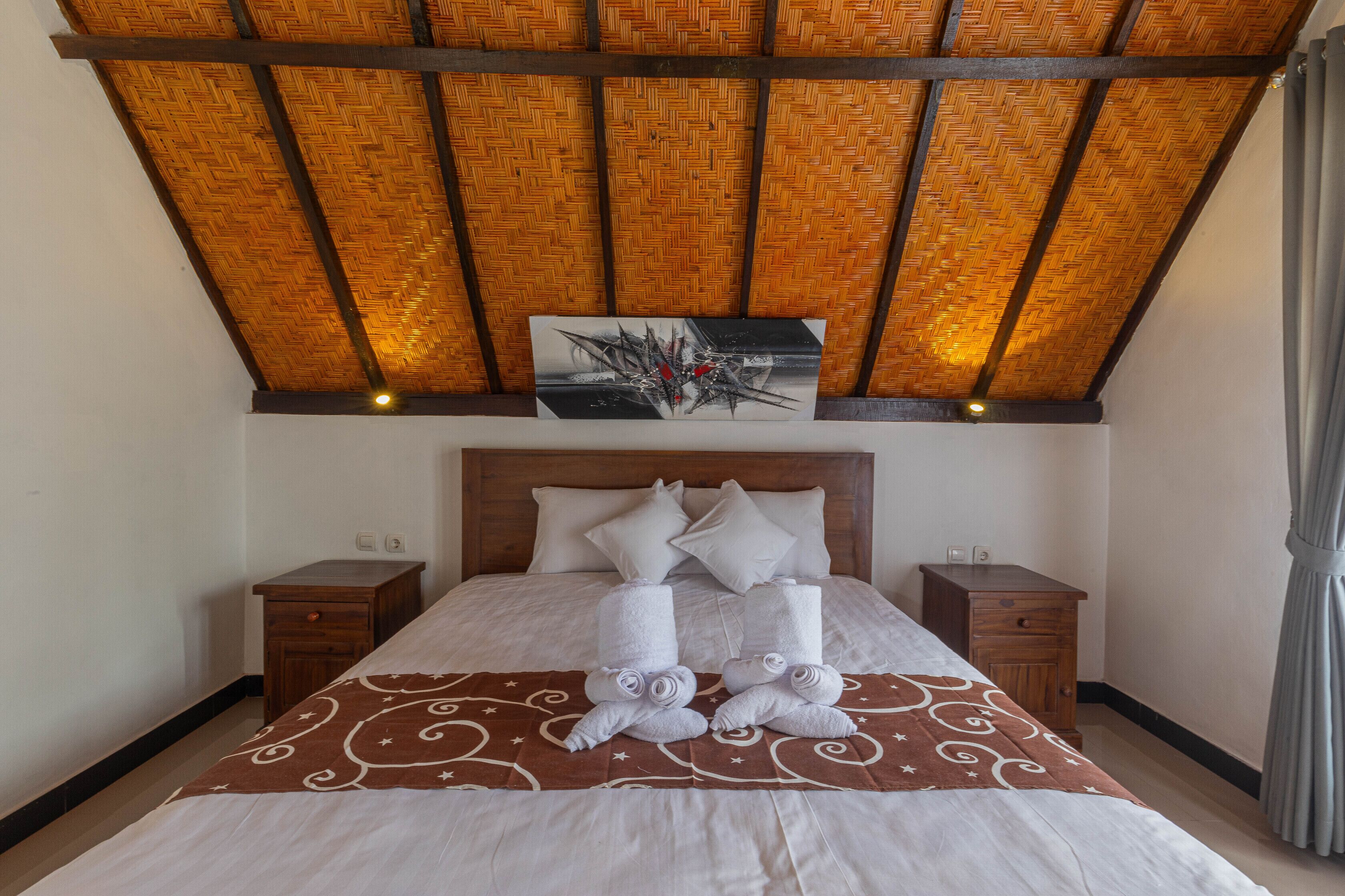 A neatly made bed with a brown patterned bedspread, two bedside tables, and a wooden headboard.