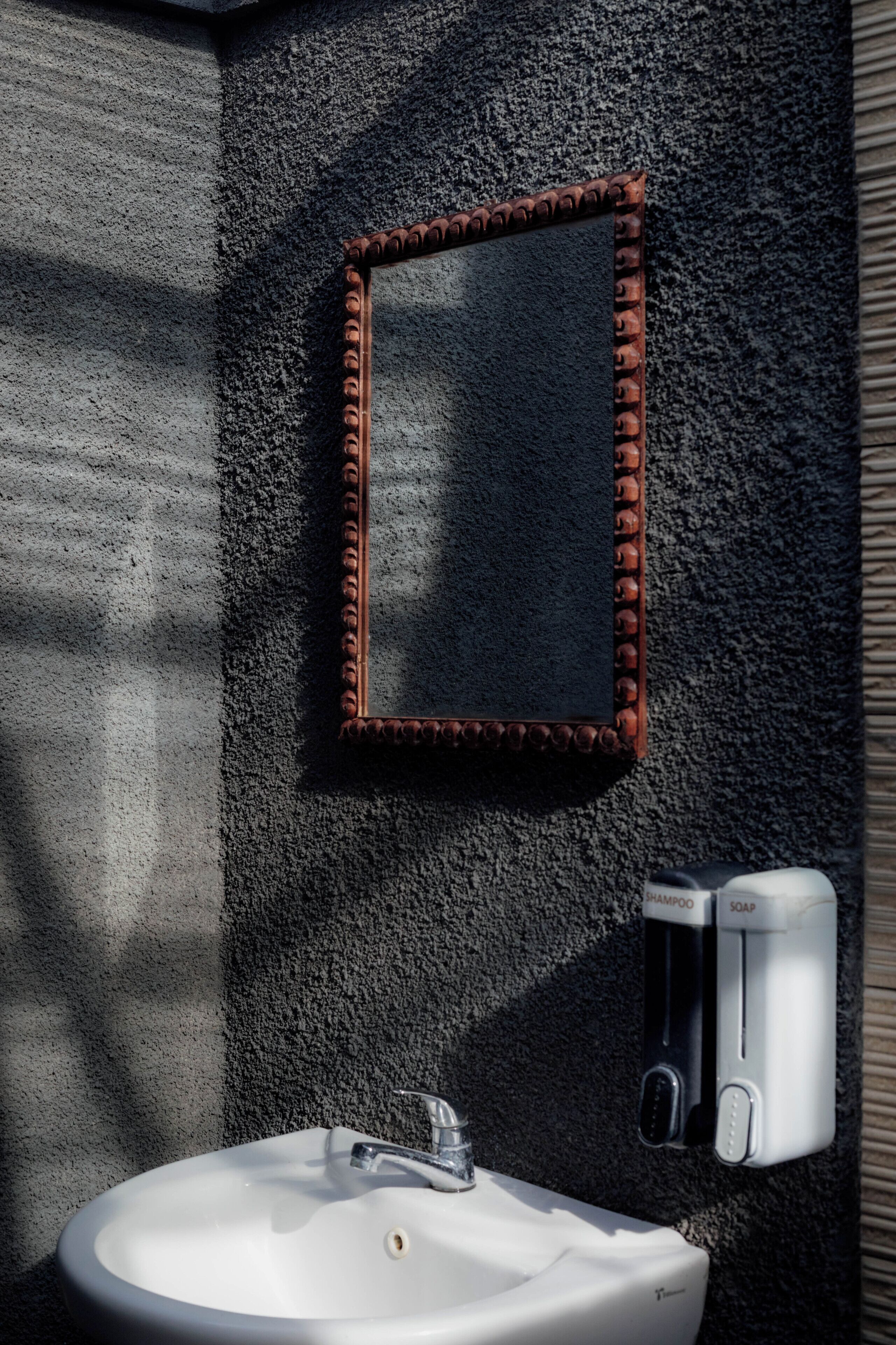 A bathroom with a white sink, a mirror with a brown frame, and a soap dispenser.
