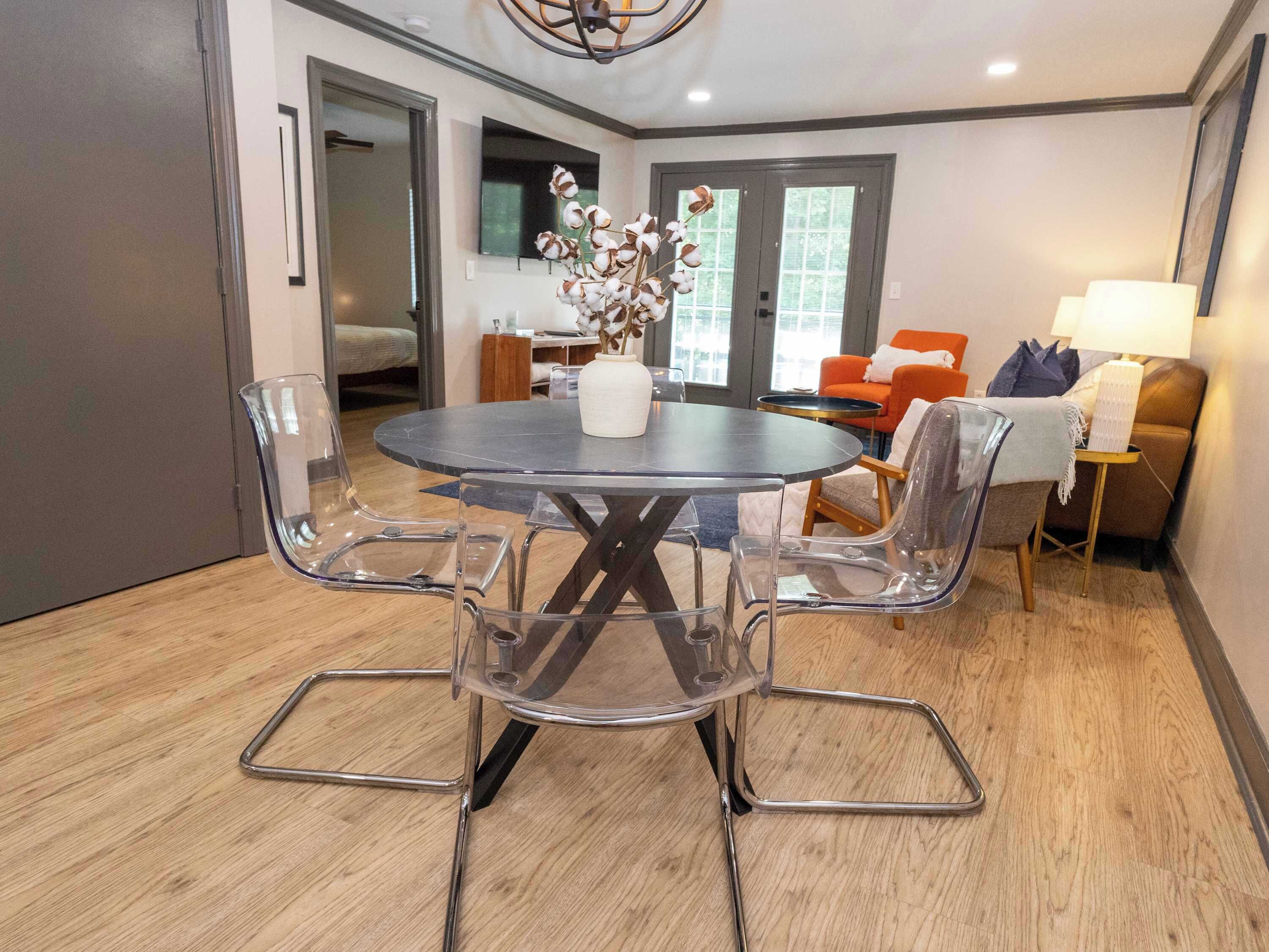 Un espace repas moderne avec une table ronde, des chaises transparentes et un vase de fleurs.