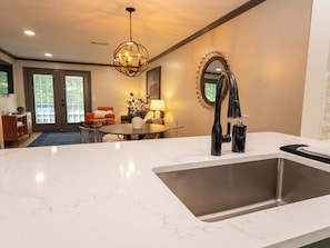 A modern kitchen with a large sink, a dining area with a table and chairs, and a living room with a sofa and a lamp.