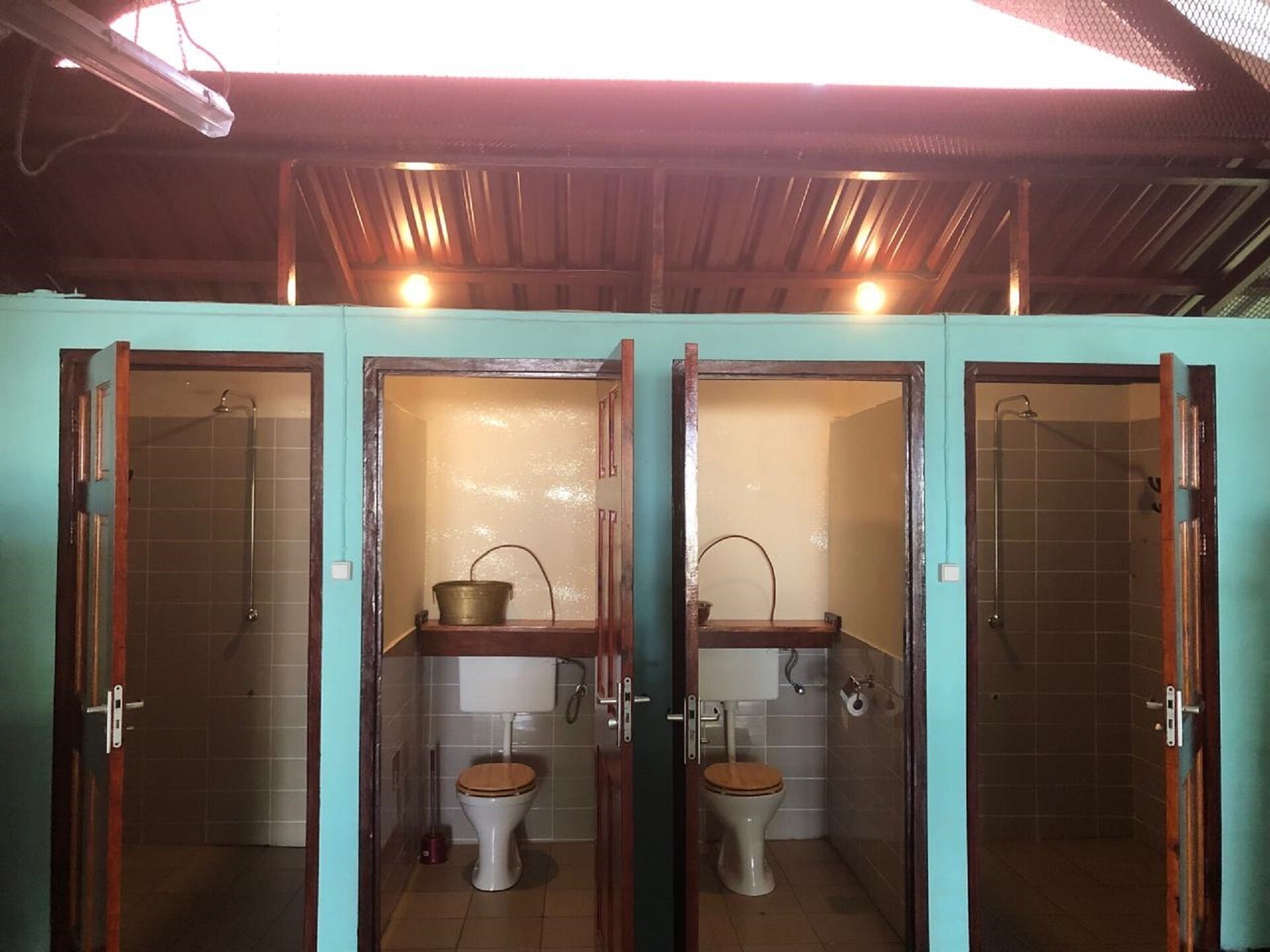 Una fila de tres baños pequeños y privados con puertas de madera y pisos de baldosas.