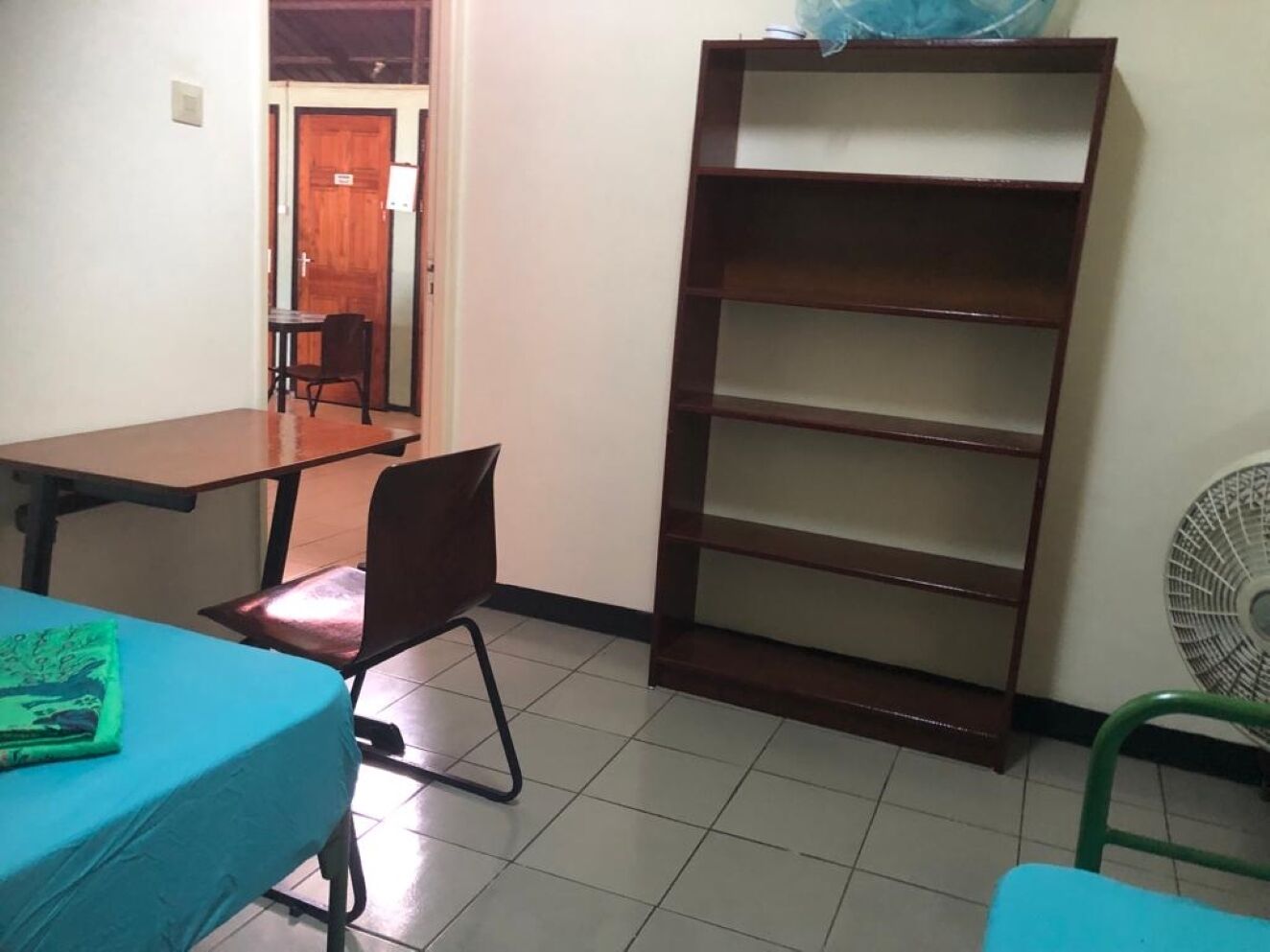 Une pièce comprenant un bureau, une chaise, une bibliothèque et un ventilateur.
