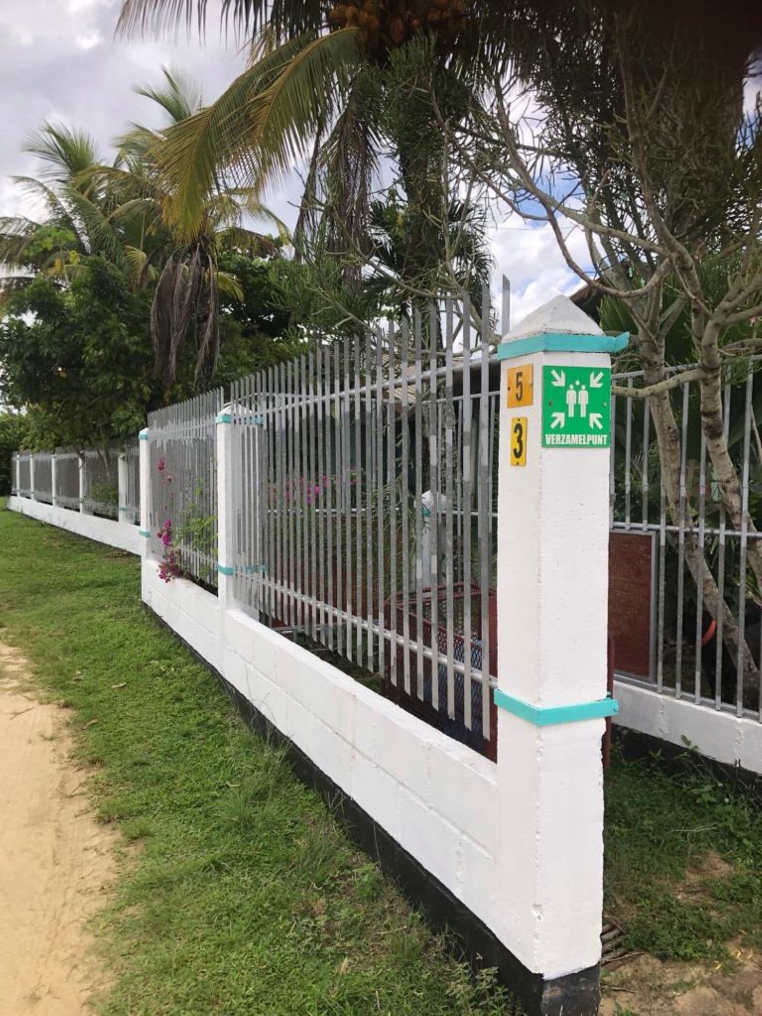 A white metal fence with a green sign indicating a public restroom.