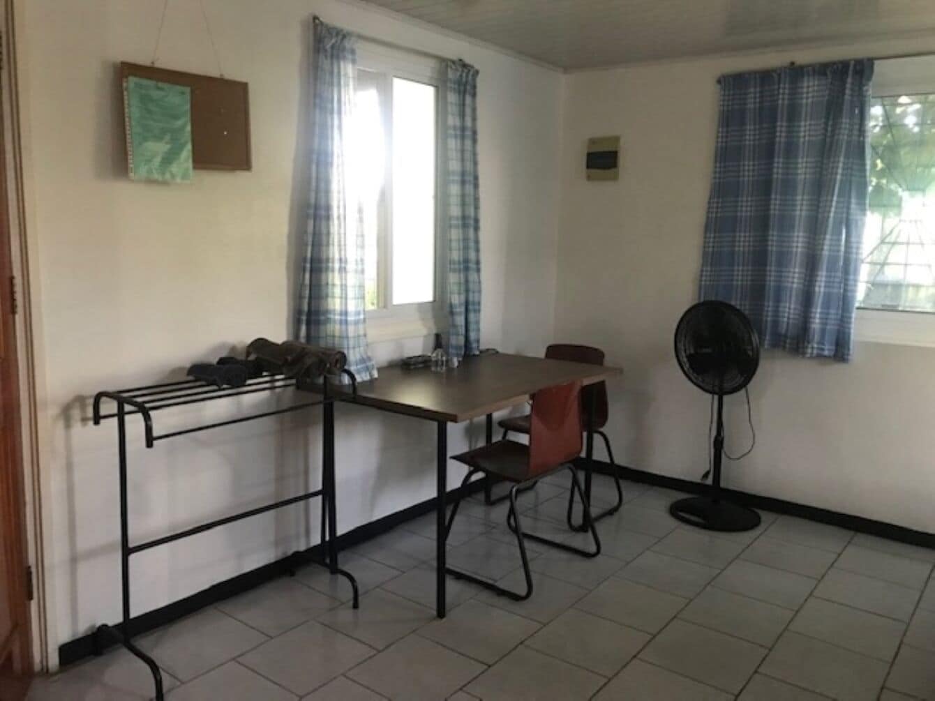 A room with a table, chairs, a fan, and a window with curtains.
