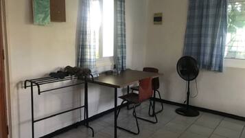 A room with a table, chairs, a fan, and a window with curtains.