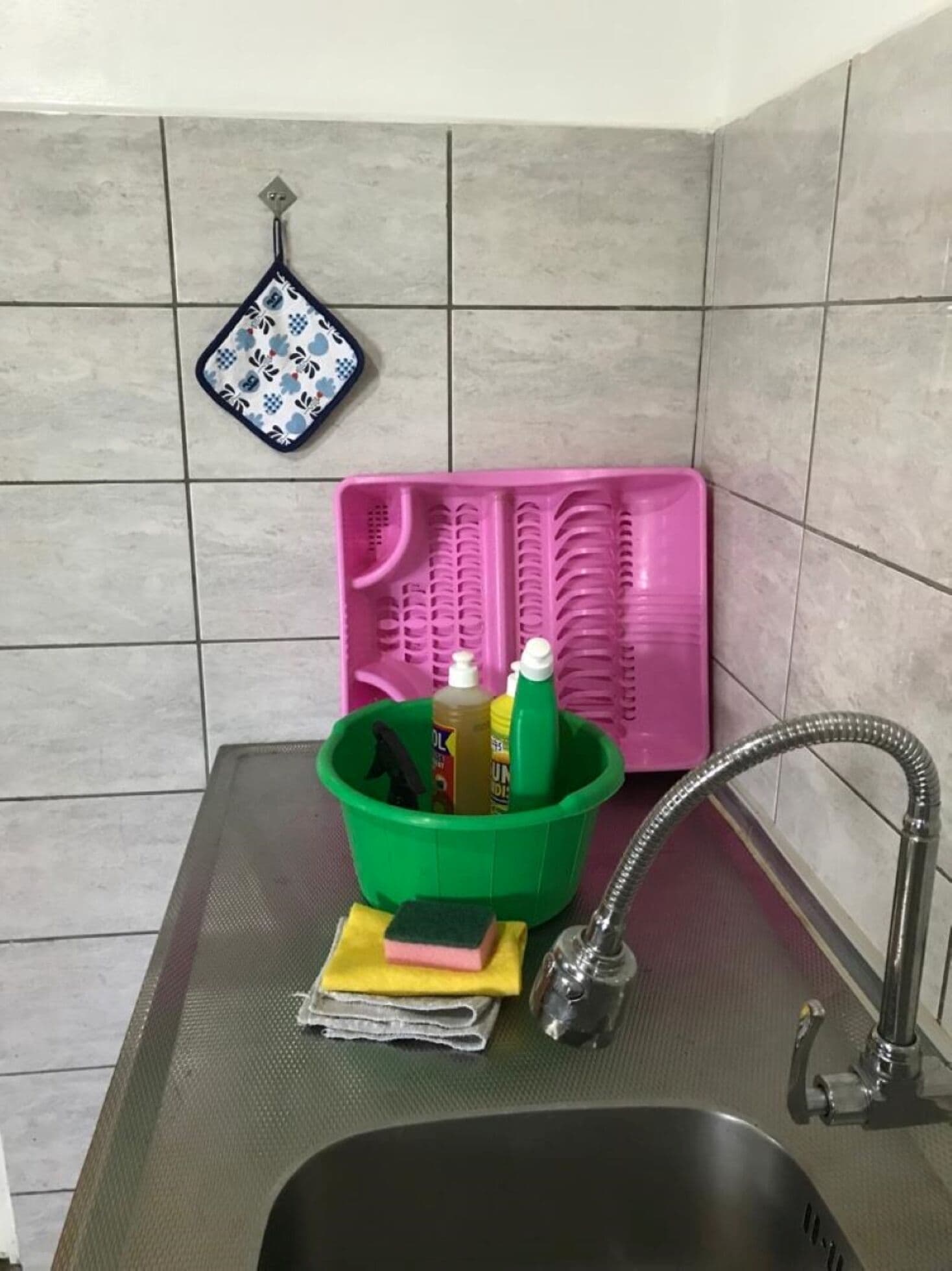 A kitchen sink with a green cleaning bucket, a pink dish rack, and a dish drying mat.