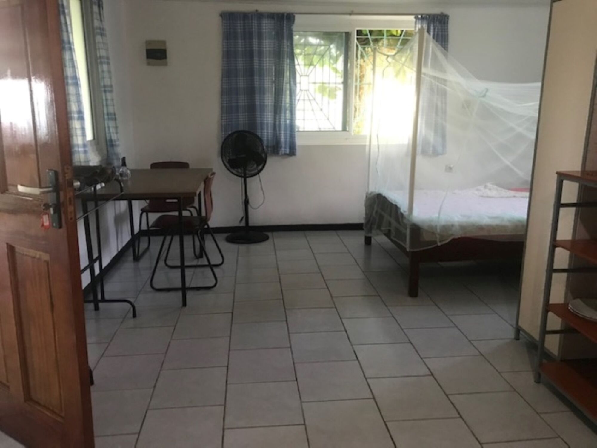 A room with a bed, a desk, a chair, a fan, and a window with curtains.