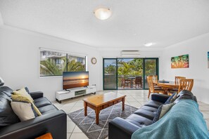 A modern living room with a TV, leather sofas, a wooden coffee table, and a balcony with a dining area.