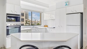 A modern kitchen with white cabinetry, a built-in microwave, an oven, and a refrigerator. There's a large window offering a view of buildings outside.