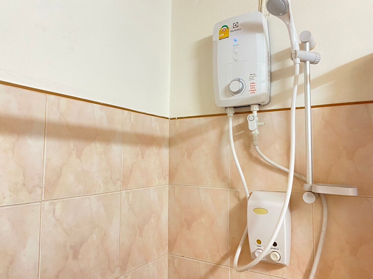 A bathroom with a white water heater mounted on the wall, connected to a showerhead and a handheld shower unit.