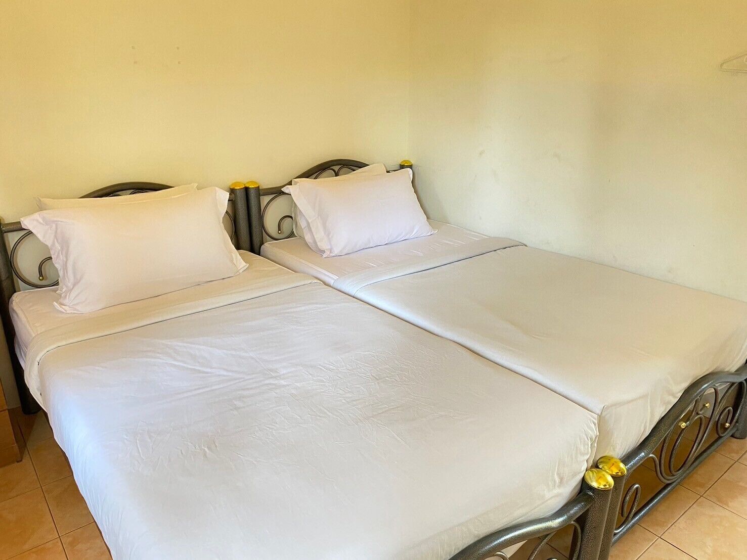 Una cama doble con sábanas blancas y estructura metálica, dos almohadas y una mesita de noche con un objeto amarillo.