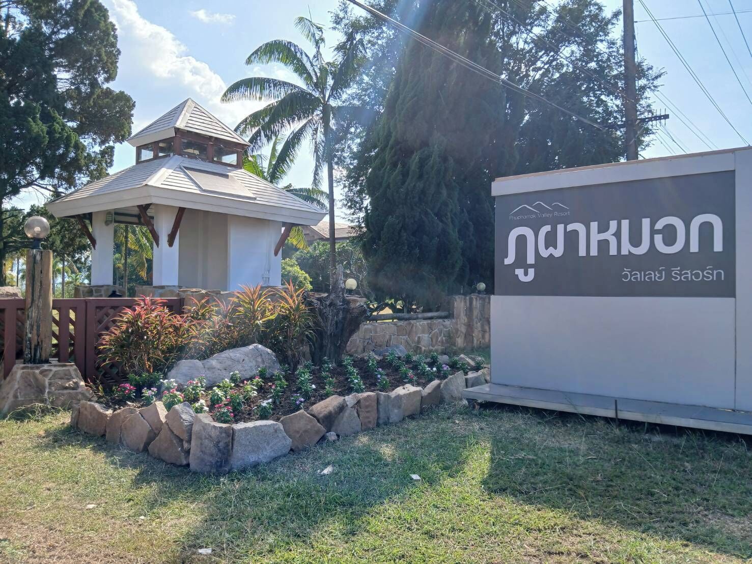 A building with a traditional architectural style, a small pavilion, and a sign with Thai script.