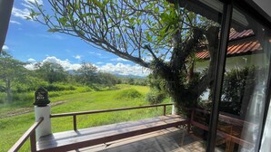 Terraza de madera con barandilla, con vistas a un paisaje verde con árboles y cielo despejado.