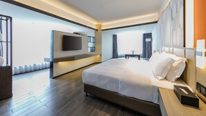 Une chambre d’hôtel moderne avec un grand lit, un téléviseur à écran plat fixé au mur et un plancher en bois.