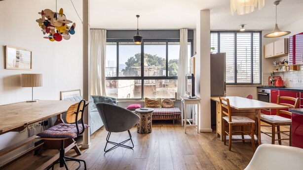 A modern kitchen with wooden countertops, a dining area with a wooden table and chairs, and a large window providing a view of the city. - Allenby Artsy Stay by Sea N' Rent (Tel Aviv)