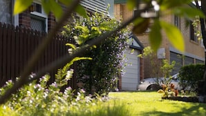A residential area with a well-maintained lawn, a wooden fence, and houses with brick exteriors. - Comfort 1-Bedroom Cottage Retreat @Yeronga (Yeronga)