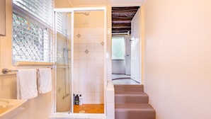 A modern bathroom with a glass-enclosed shower, a wooden floor, and a staircase leading to another room. - Comfort 1-Bedroom Cottage Retreat @Yeronga (Yeronga)