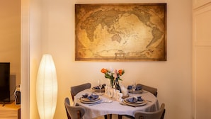 A dining area with a round table set for six, a large world map on the wall, and a tall floor lamp. - Comfort 1-Bedroom Cottage Retreat @Yeronga (Yeronga)