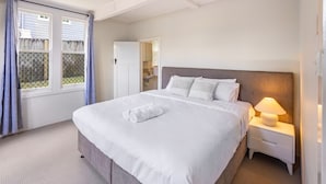 A neatly made bed with white linens and a rolled towel, a bedside lamp, and a window with curtains. - Comfort 1-Bedroom Cottage Retreat @Yeronga (Yeronga)