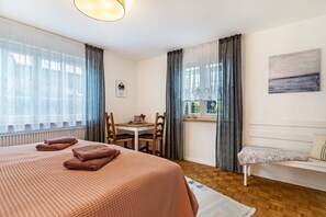 Hotellihuone, jossa on sänky, työpöytä, tuoli, penkki ja ikkuna, jossa on verhot.