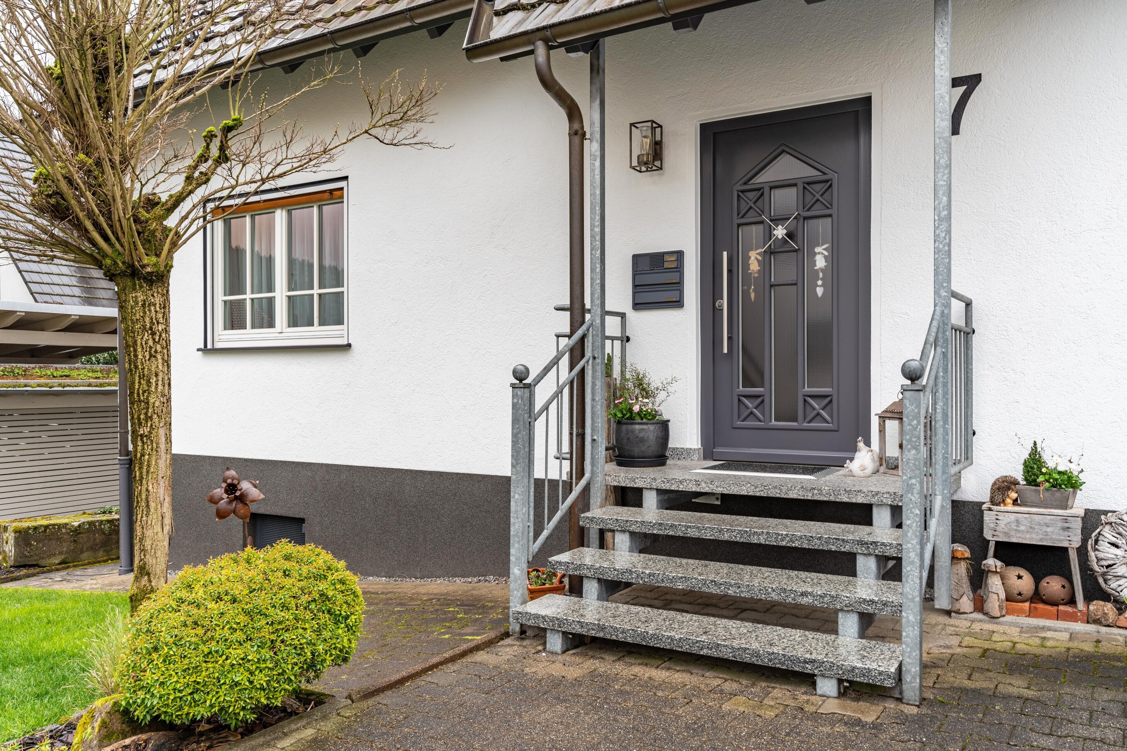 A house with a dark front door, a small porch with steps, and a potted plant on the steps.