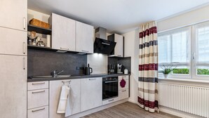 Une cuisine moderne avec des meubles de couleur claire, une hotte noire, un four encastré et une fenêtre agrémentée de rideaux à rayures.