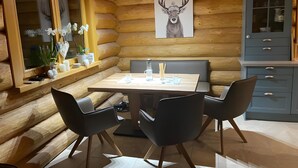 Interior de una cabaña de troncos con una mesa de comedor, sillas, un armario y una obra de arte con ciervo.