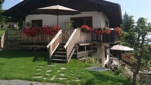 A two-story building with a balcony, a wooden staircase, and a covered area with an umbrella. - Holiday Apartment "Haus Weitblick 2" near Slopes with Private Terrace & Wi-Fi (Hochrindl)
