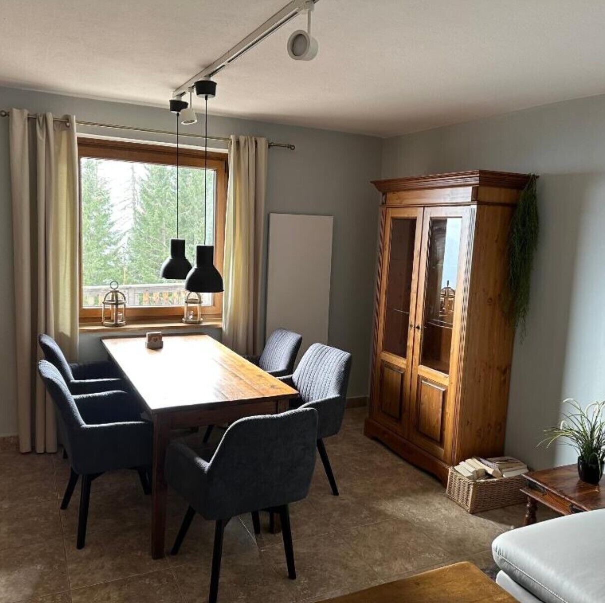 A dining area with a wooden table, four chairs, a cabinet, and a window with curtains.