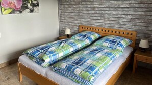 Un lit double avec une couvre-lit à carreaux, deux tables de chevet avec des lampes, une tête de lit en bois et un mur orné d’un tableau floral.