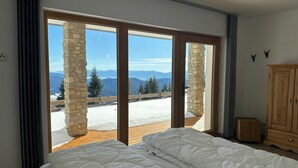A bedroom with a large bed, a wooden floor, stone pillars, and a view of mountains through glass doors. - Chalet "Reimers 2a" with Mountain View, Private Terrace & Wi-Fi (Hochrindl)