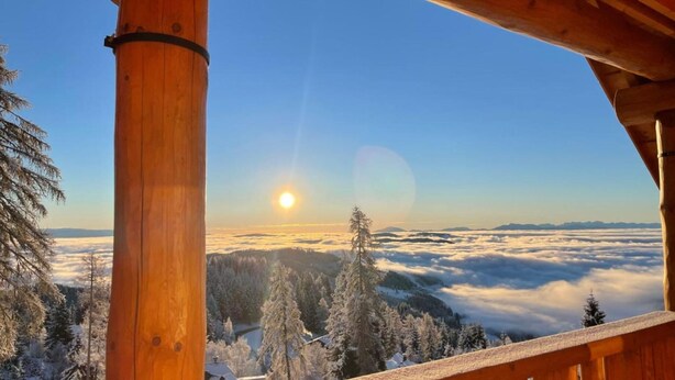 A wooden cabin with a view of a snowy landscape and a sun setting or rising over the horizon. - Chalet "Reimers 2a" with Mountain View, Private Terrace & Wi-Fi (Hochrindl)