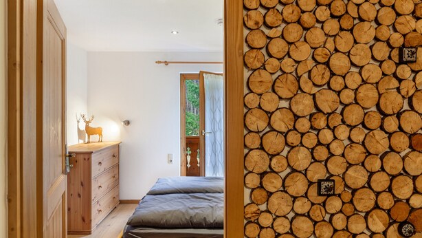 Un dormitorio con cama, cómoda de madera y una pared de leña apilada.