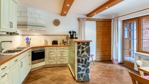 Una cocina con armarios blancos, una isla de piedra y un techo de madera.