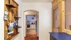 Un pasillo estrecho con paredes de madera, una puerta de madera a la derecha y una cocina visible a través de un arco.