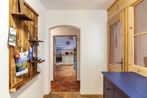 Un couloir étroit aux murs en bois, une porte en bois sur la droite et une cuisine visible à travers une arche.