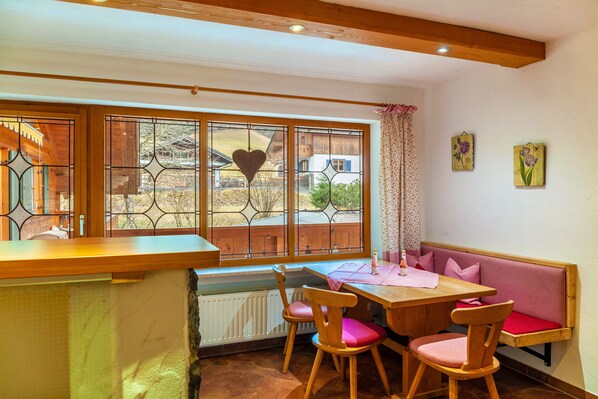 Une pièce chaleureuse avec une table en bois, des chaises, un banc et une grande fenêtre donnant sur l’extérieur.
