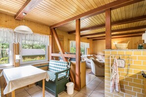 Un intérieur en bois comprenant une table, un banc et un coin cuisine avec des ustensiles suspendus.