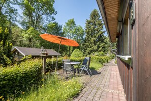 Une terrasse avec une table et des chaises, un parasol orange et une mangeoire à oiseaux.