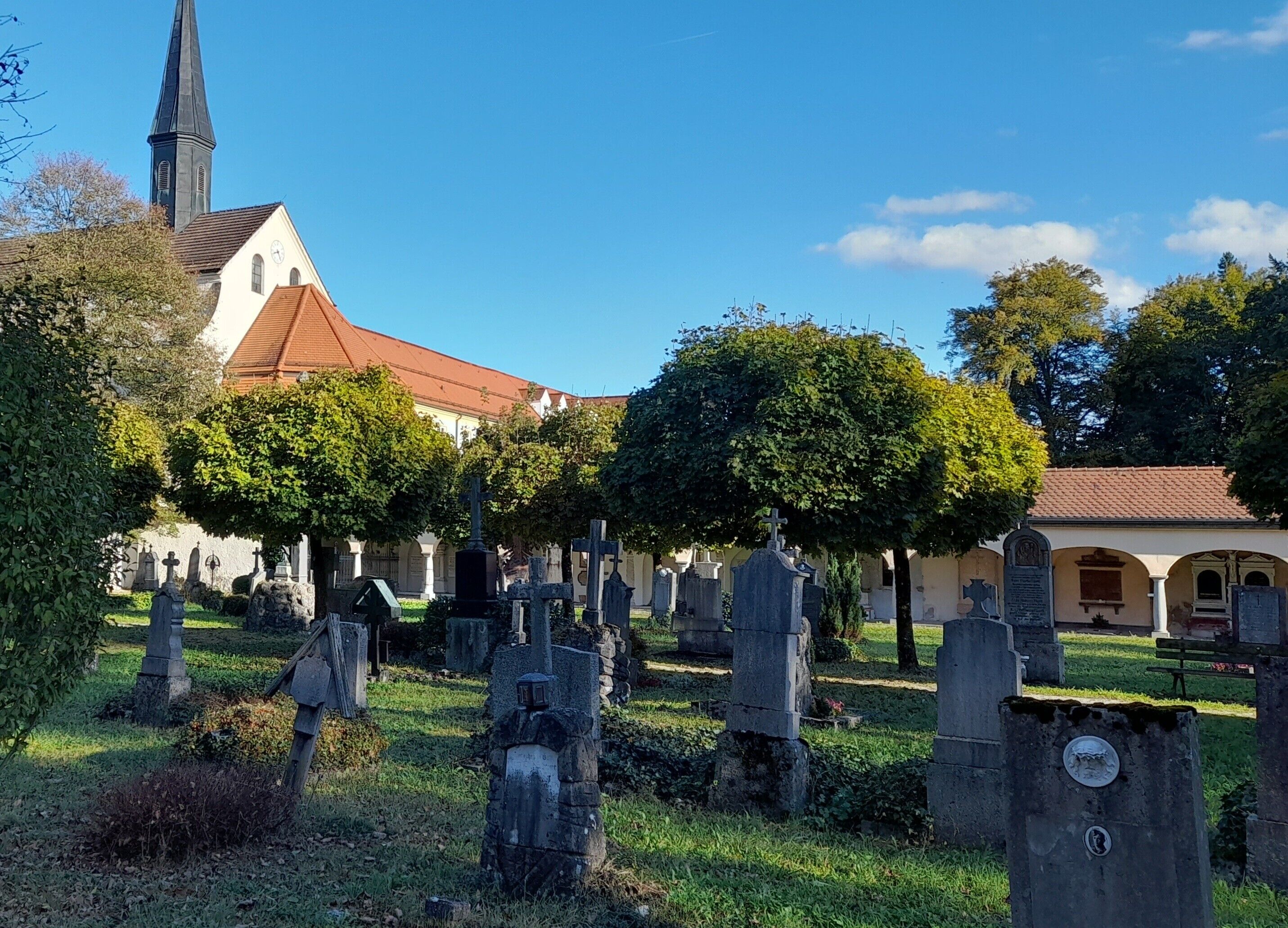 Un cimetière avec des pierres tombales, une église avec un clocher et un bâtiment avec un toit rouge.